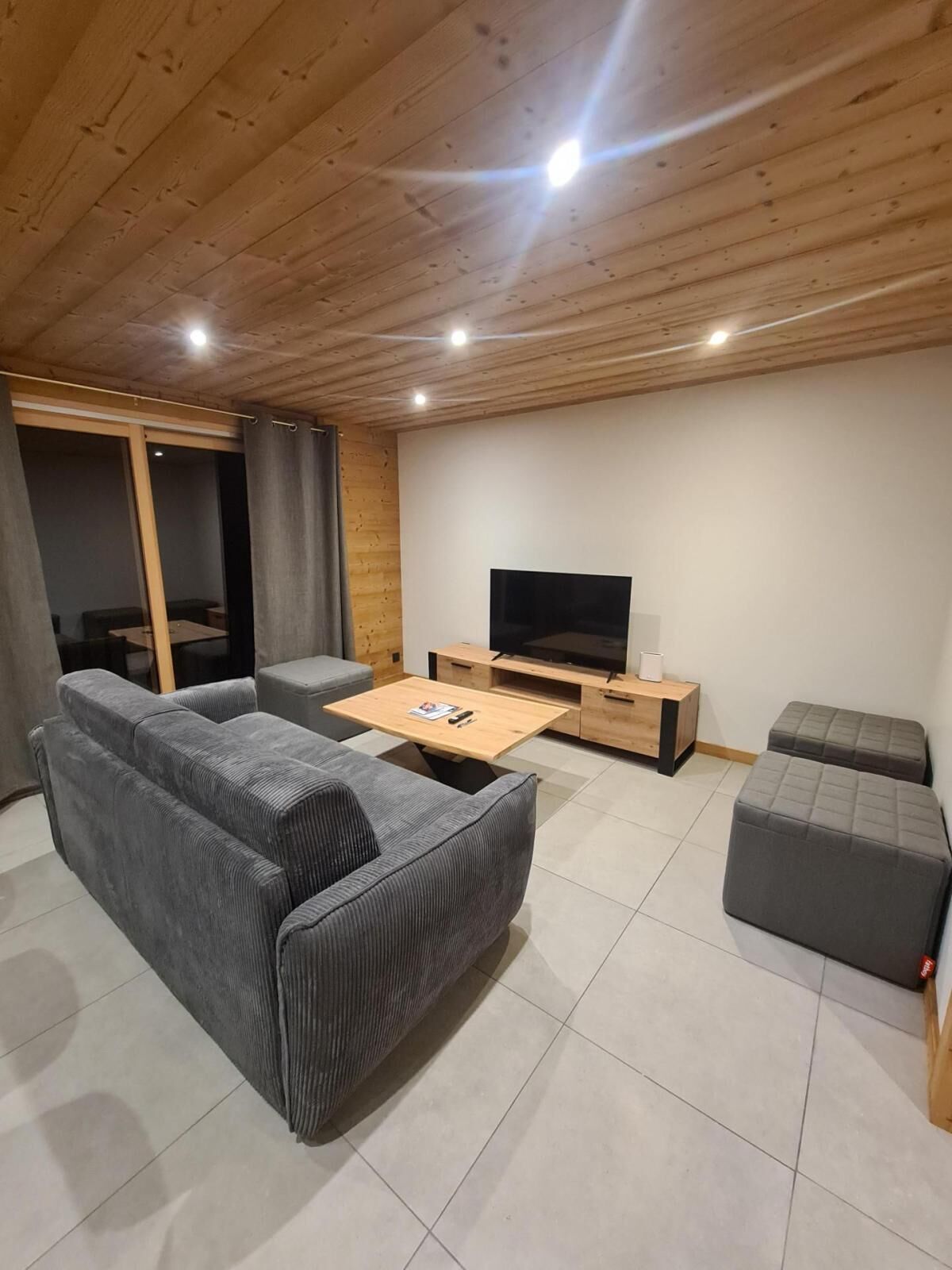 Un salon moderne avec un canapé gris, une table basse en bois, un téléviseur et un petit meuble en bois.