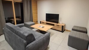 Ein modernes Wohnzimmer mit einem grauen Sofa, einem Holztisch, einem Fernseher und einer kleinen Holzkommode.