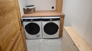 Ein Waschraum mit zwei Waschmaschinen, einer Holzbänke und einem Tisch mit einem Wäschekorb.