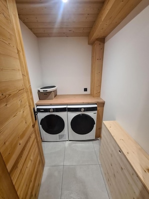 A laundry room with two front-loading washing machines, a wooden bench, and a small table with a basket.