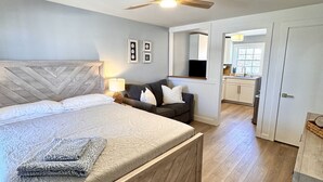 Une chambre moderne avec un grand lit, un ventilateur de plafond et une vue sur la cuisine.