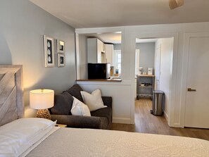 Een slaapkamer met een bed, een nachtkastje met een lamp, een bank en een televisie in de aangrenzende kamer.