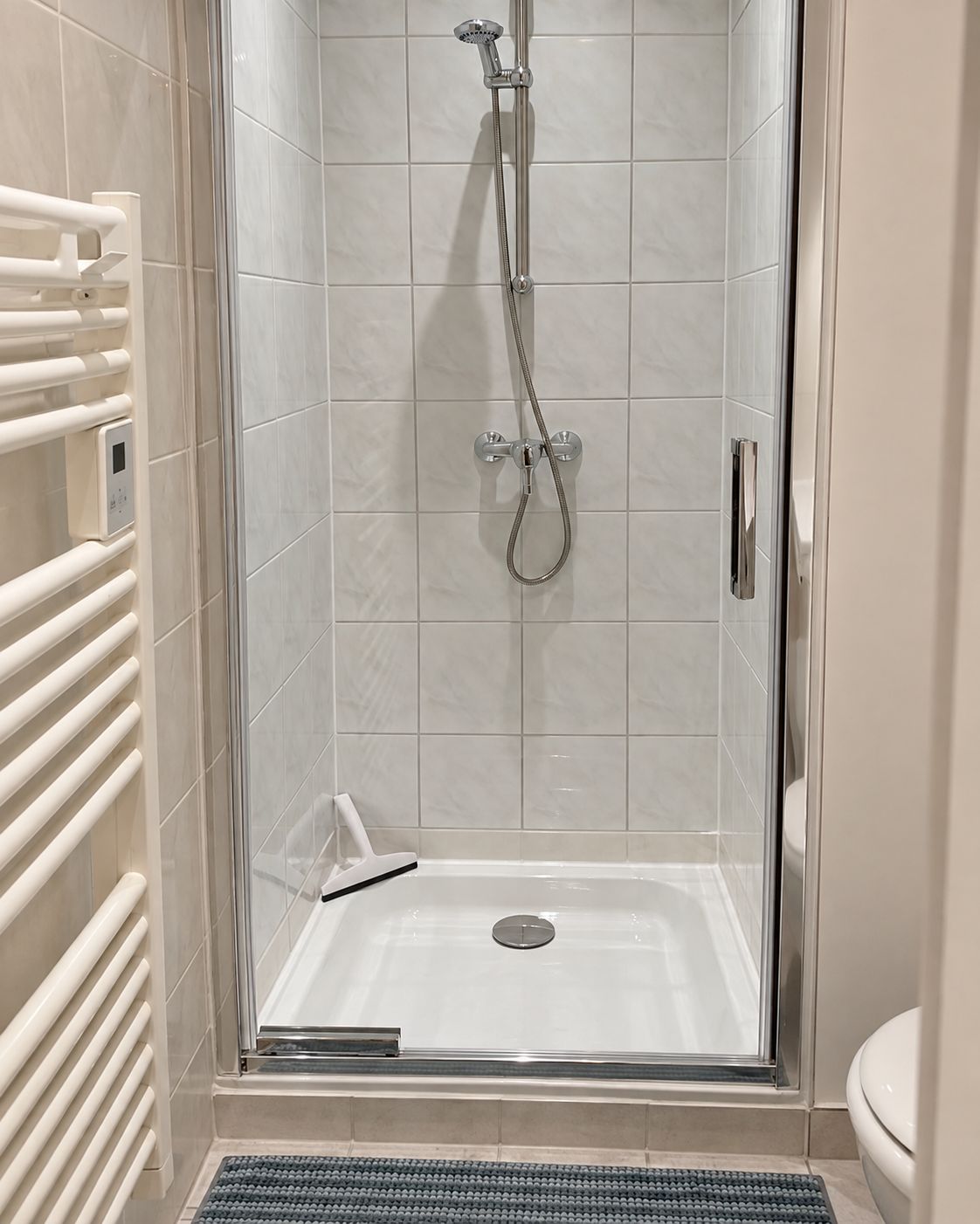 Eine begehbare Dusche mit Glastür, Bedienfeld und weiß gefliestem Boden.