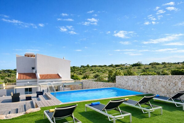 A modern pool area with a clear blue pool, lounge chairs, and a white building with a red-tiled roof. - Cruzeiro by Check-in Portugal (Quarteira)