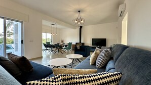 A modern living room with a grey sofa, a coffee table, and a dining area with chairs and a TV. - Cruzeiro by Check-in Portugal (Quarteira)