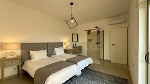 A bedroom with two beds, a bedside table with a lamp, a mirror, a shower, and an air conditioning unit. - Cruzeiro by Check-in Portugal (Quarteira)