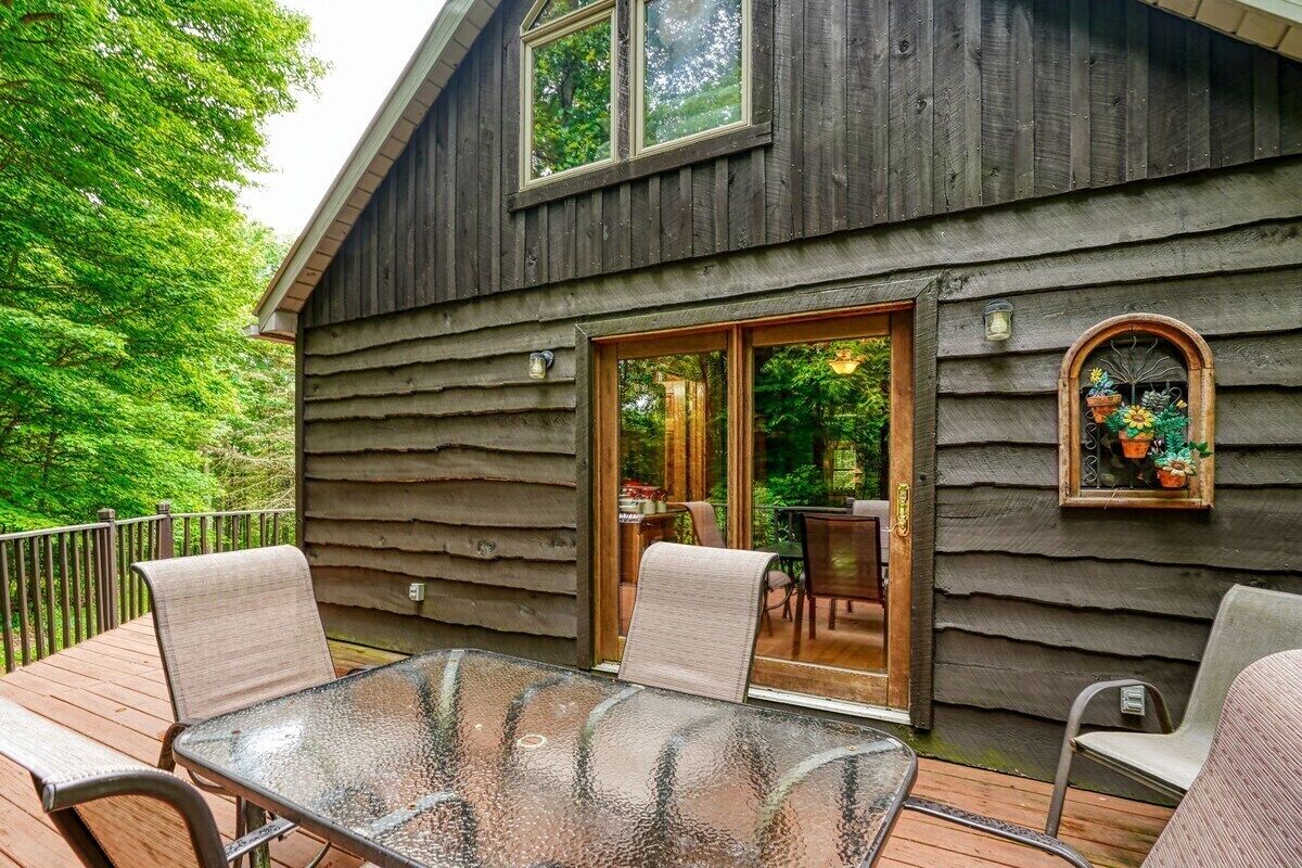 Eine Holzhütte mit einer verglasten Terrasse, Sitzgelegenheiten im Freien und Blick auf einen üppigen Garten.