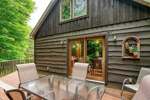 A wooden cabin with a glass-enclosed patio, outdoor seating, and a view of a lush garden.