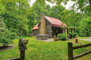 A rustic cabin with a stone chimney, surrounded by lush greenery and a wooden deck.