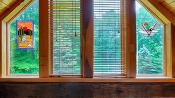 A room with a large window featuring wooden blinds, a stained glass window with a desert scene, and a view of green trees.