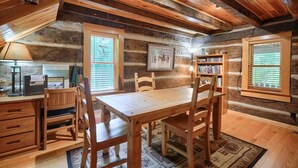 Un interior rústico de madera con una mesa de comedor, sillas, una estantería y un cuadro en la pared.