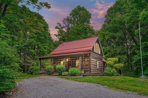 A rustic log cabin with a red roof, surrounded by lush greenery and trees.