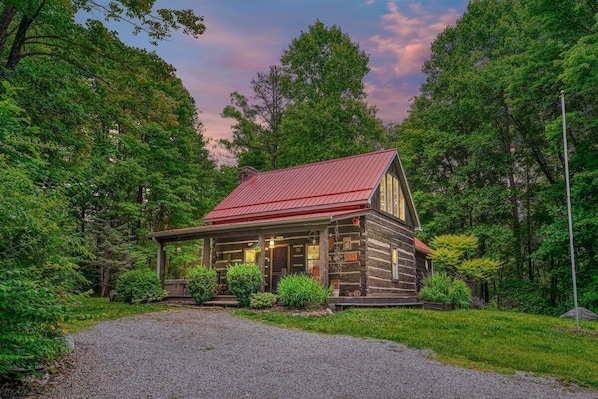 A rustic log cabin with a red roof, surrounded by lush greenery and trees.