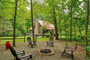 Eine Holzhütte, umgeben von einem Wald, mit Kiesfläche und vier Adirondack-Stühlen.