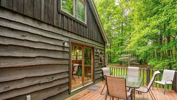 Una cabaña de madera con terraza, puertas correderas de vidrio y mobiliario exterior.