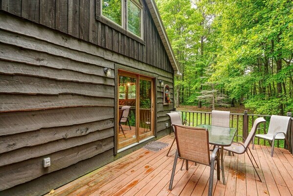 A wooden cabin with a deck, glass sliding doors, and outdoor seating.