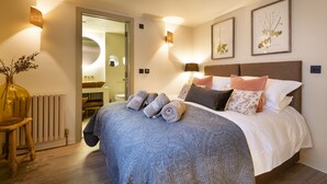 A neatly made bed with rolled towels, a wooden chair, and wall-mounted lamps. - Solace | Finest Stays (Totnes)