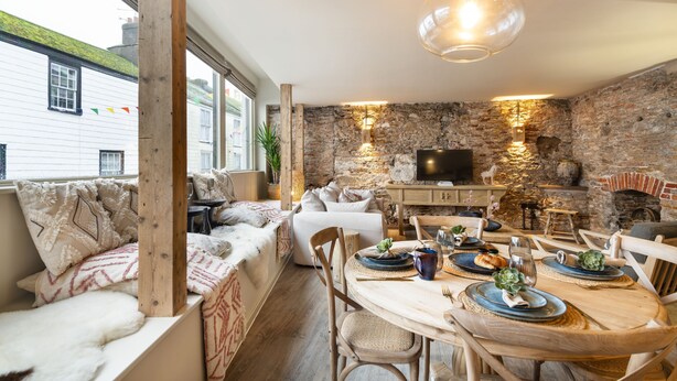 A cozy dining area with a stone wall, wooden furniture, and a television. - Solace | Finest Stays (Totnes)
