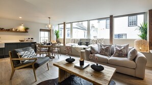 A modern living room with a sofa, a wooden coffee table, and a dining area with chairs and a table. - Solace | Finest Stays (Totnes)