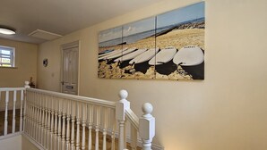 A hallway with a white railing, a door, and a beach-themed painting on the wall.