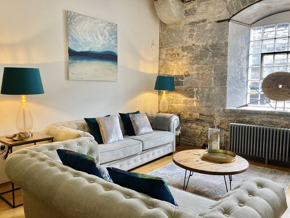 Ein Wohnzimmer mit Steinwand, einem weißen Sofa, einem runden Holztisch und zwei Lampen.