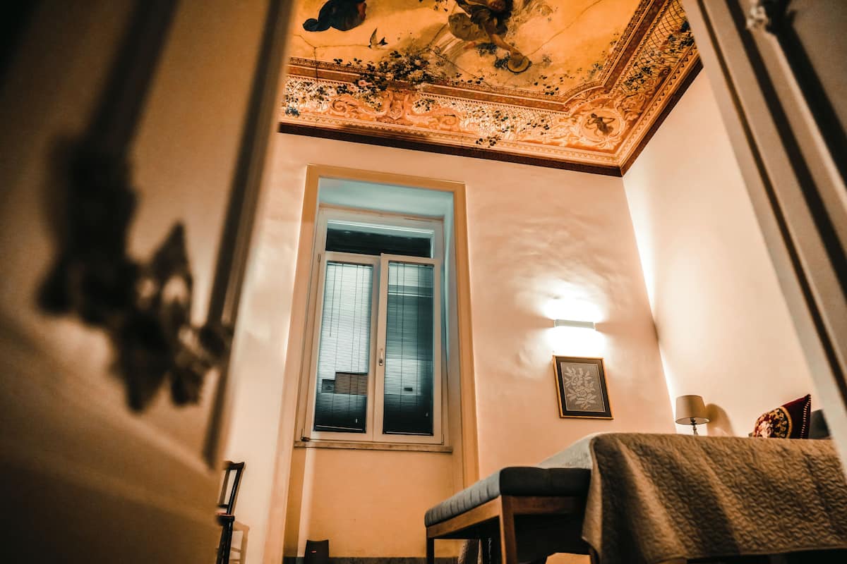 Una habitación con un ventanal grande, un cuadro en la pared y una lámpara sobre una mesita.