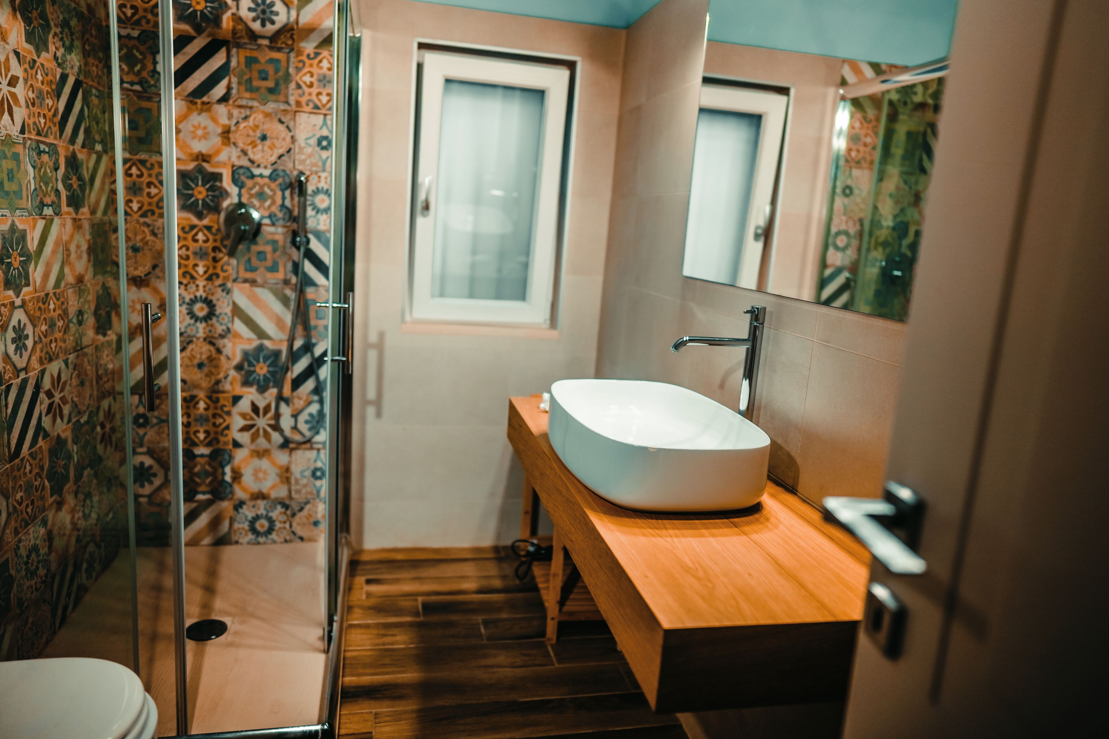 Ein Badezimmer mit einem Holzbadezimmer, einem weißen Waschbecken und einer Dusche mit gemusterten Fliesen.