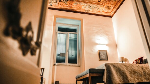 Una habitación con cama, un banco, una ventana y una lámpara.