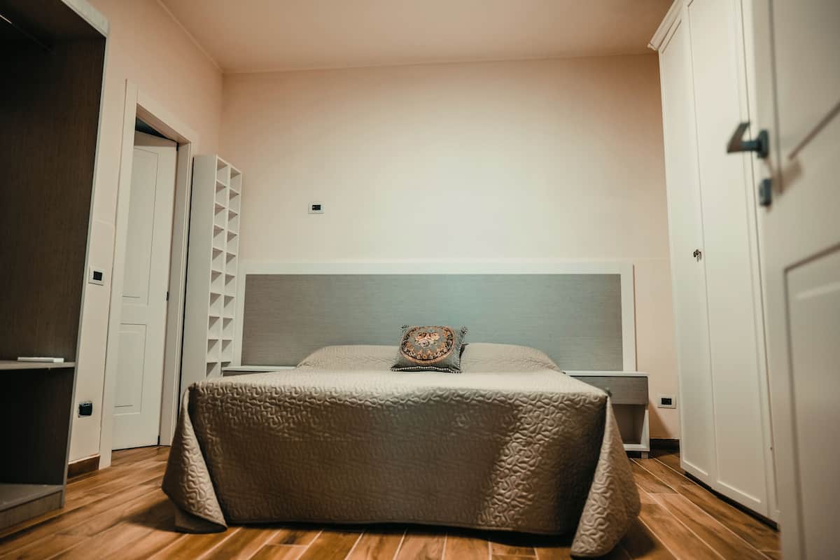 Un dormitorio con una cama grande, una mesita de noche, un armario y una puerta que da a otra habitación.