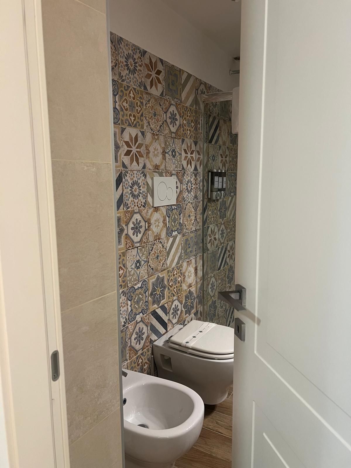 Een badkamer met betegelde wand, twee toiletten en een douchetoilet.