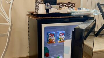A compact refrigerator with a coffee maker and a tray of snacks. Inside, there are cartons of milk and a bottle of juice.