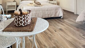 Un dormitorio con una cama grande, dos mesitas de noche, una mesa redonda con una cesta de pan y suelo de madera.