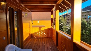 Une terrasse en bois avec une chaise en plastique blanche, des rampes en bois et une vue sur une montagne et des bâtiments.