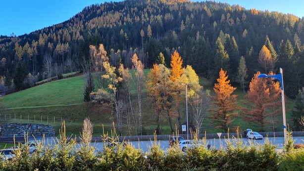 Un espace de stationnement avec des voitures, une structure en pierre et une colline bordée d’arbres.