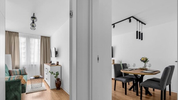 A modern living room with a sofa, a coffee table, and a TV. There is a dining area with a table and chairs.