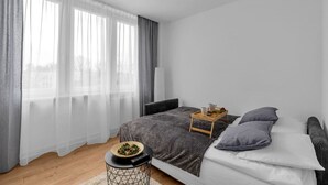 A modern bedroom with a bed, bedside table, and a window with sheer curtains.