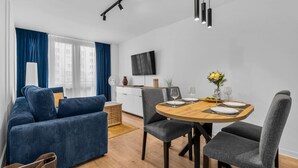 A modern living room with a blue sofa, grey armchairs, and a wooden dining table set for two.