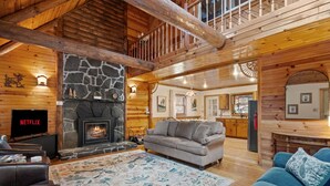 A cozy cabin interior with a stone fireplace, a grey sofa, and a television displaying 'NETFLIX'. - Lucky Log Cabin- Hottub fireplace 12min to Mt Snow (Wardsboro)