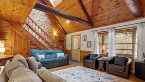 A cozy cabin interior with a wooden staircase, a blue sofa, a brown leather chair, and a floral rug. - Lucky Log Cabin- Hottub fireplace 12min to Mt Snow (Wardsboro)