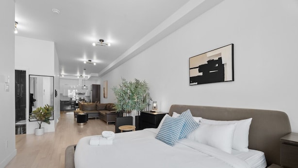 Un dormitorio moderno con una cama grande, una mesita de noche, un espejo, una planta en maceta y vistas al área de estar.