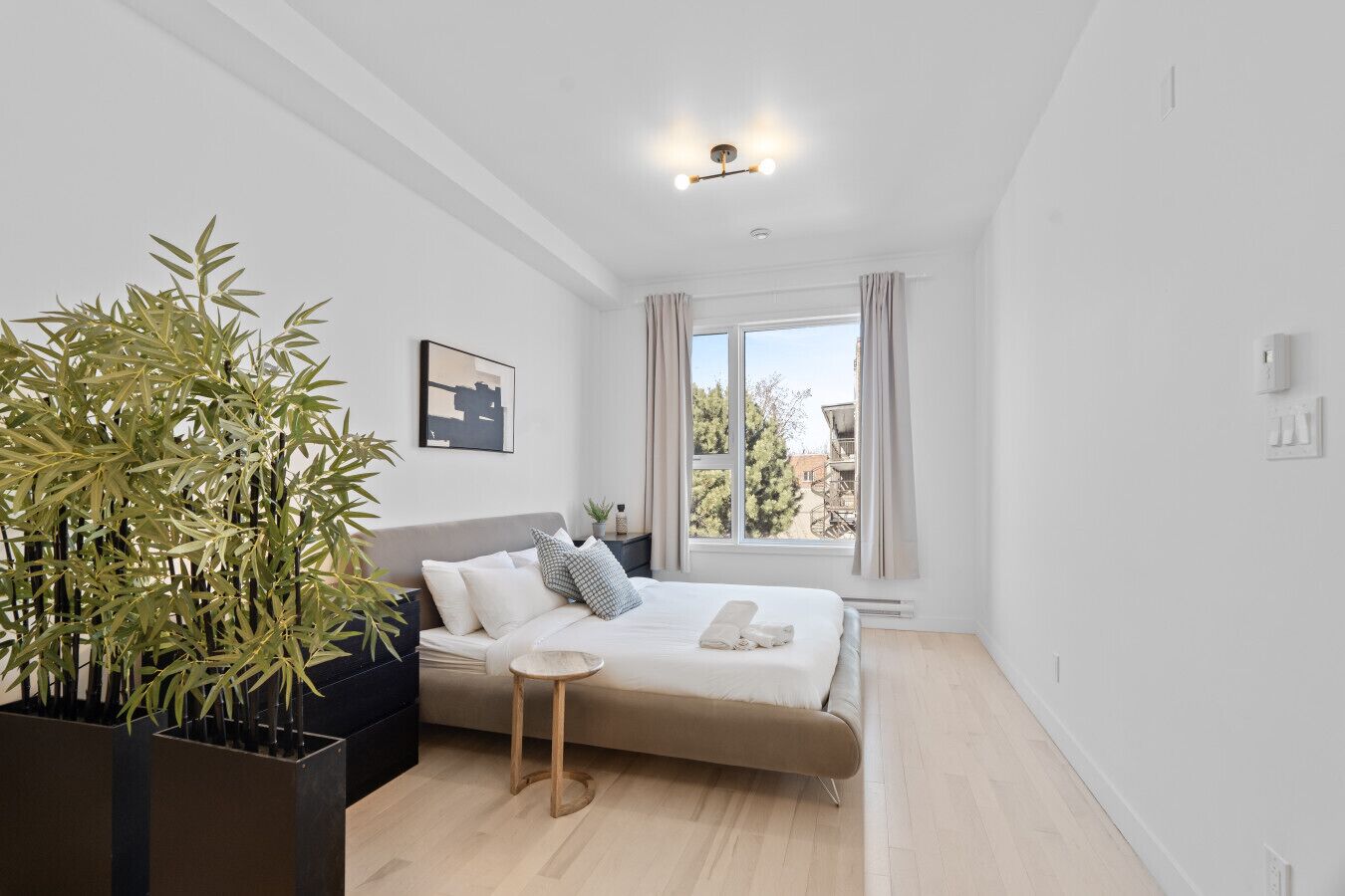A modern bedroom with a bed, bedside table, and a large window.