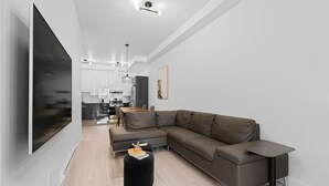Una sala de estar moderna con un sofá modular, un televisor de pantalla plana, una mesa de centro redonda negra y una zona de comedor minimalista.