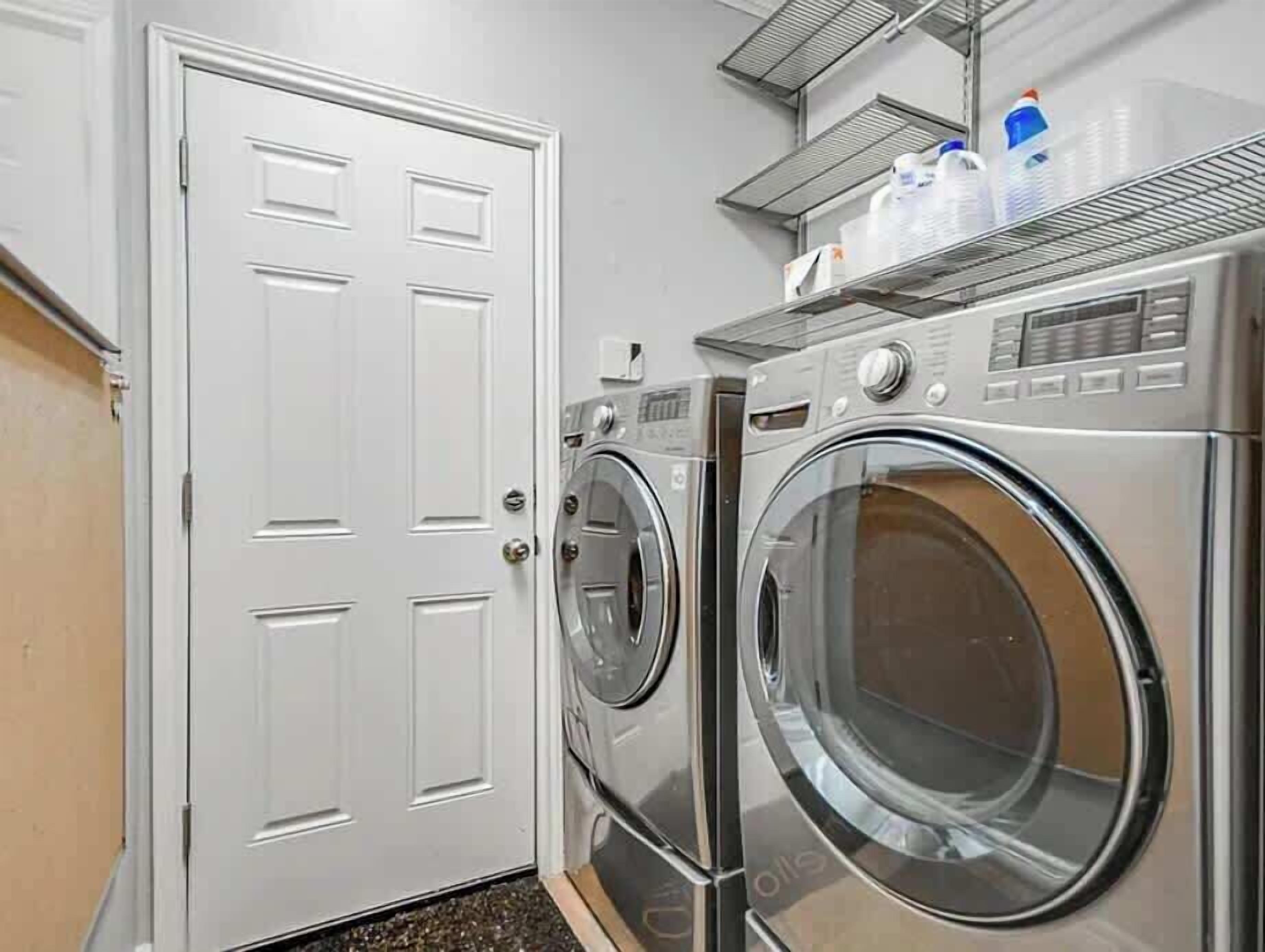 A laundry room with two front-loading washing machines, a white door, and a metal shelf above the machines.