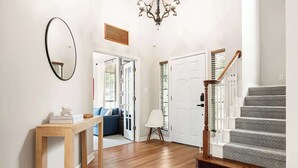 A hallway with wooden flooring, a mirror, a chandelier, a staircase with a wooden handrail, and a blue sofa in the background. - Walk to Zilker Barton Springs 5BR 3BA Villa Sleeps 14 (Austin)