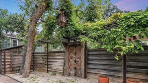 A wooden fence with a decorative gate, two terracotta pots, and a tree in a backyard. - Walk to Zilker Barton Springs 5BR 3BA Villa Sleeps 14 (Austin)