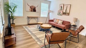 A living room with a wooden floor, a pink sofa, a round coffee table, and a ceiling fan. - Villa in Zilker - Peaceful Stylish Home with Yard (Austin)