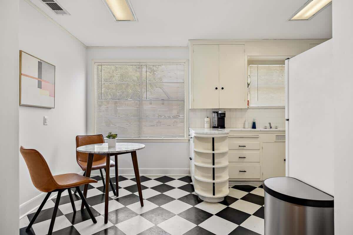 A compact kitchen with a checkered floor, a dining table with chairs, and white cabinetry.