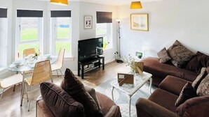 Una sala de estar moderna con un sofá marrón, una mesa de comedor con sillas, un televisor y una lámpara.