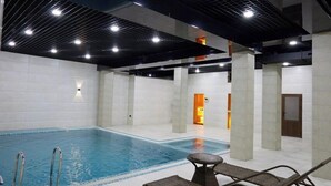 An indoor swimming pool with clear water, surrounded by tiled flooring and a ceiling with black grid patterns. - Noble Samarkand (Samarkand)