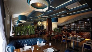 A restaurant with a blue leather booth, wooden tables, and hanging pendant lights. - Noble Samarkand (Samarkand)